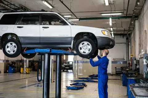 Un mécanicien en bleu vérifie une voiture sur un pont élévateur. C'est le contrôle technique d'une voiture neuve de 5 ans.