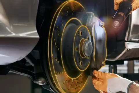 Inspection d'un frein de service de voiture. Un mécanicien utilise une lampe torche pour examiner le disque et l'étrier.
