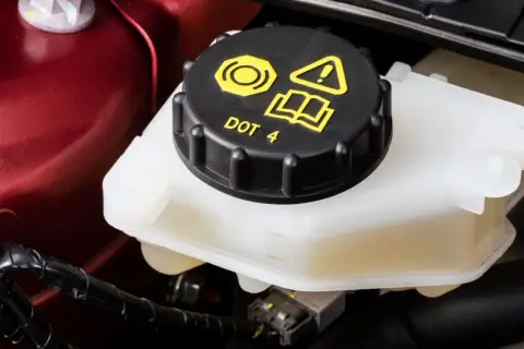 Réservoir de liquide de frein DOT 4, le niveau est visible sur le côté du récipient blanc.