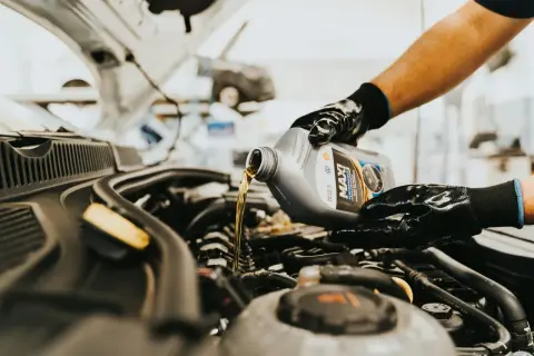 Main d'un mécanicien versant de l'huile neuve dans le moteur d'une voiture diesel. L'entretien régulier est essentiel pour la vidange de votre voiture diesel.