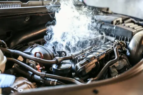 Fumée épaisse s'échappe d'un moteur de voiture, suggérant un bruit de cliquetis moteur diesel inquiétant.