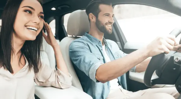 Un jeune homme souriant conduit, sa compagne à ses côtés, profitant de la **conduite supervisée accompagnateur**.
