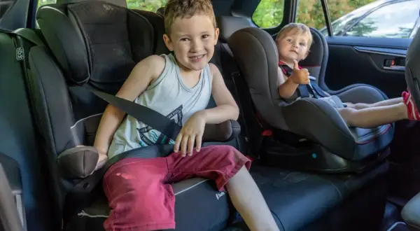 Deux enfants souriants dans leurs sièges auto, prêts pour le transport en voiture. Le plus grand fait un clin d'œil, le plus jeune montre son pouce levé.