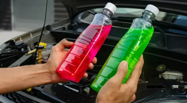Deux bouteilles de liquide de refroidissement, une verte et une rose, sont tenues devant le moteur d'une voiture. Quel liquide de refroidissement vert pour quelle voiture ?