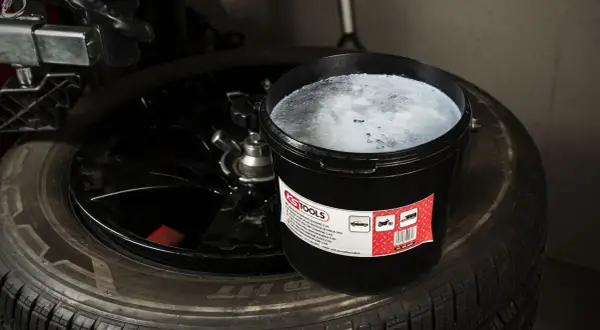 Un seau de pâte pour monter les pneus, vis dans pneu, est posé sur un pneu noir.