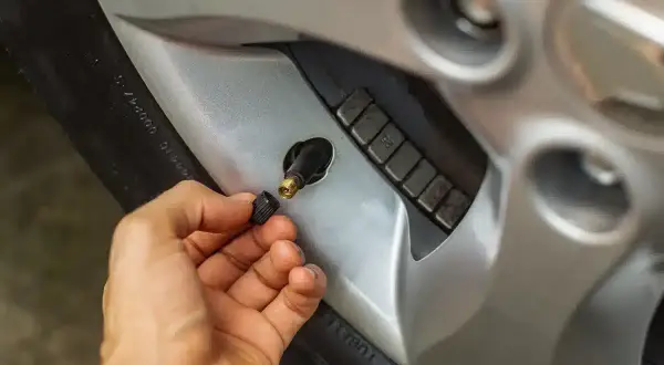 Main d'une personne retirant le capuchon d'un valve pneu qui fuit, révélant le mécanisme de la valve.