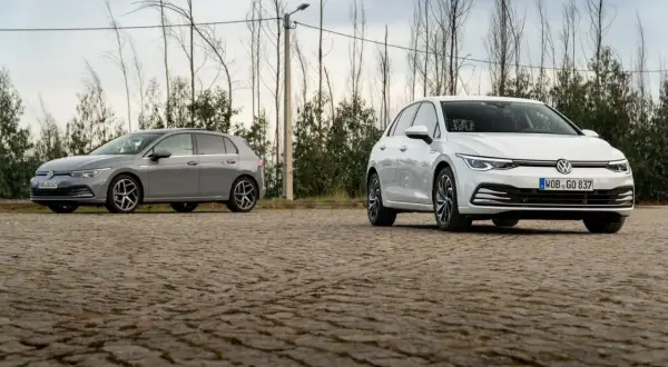 Deux Volkswagen Golf 8, une grise et une blanche, stationnées sur un sol pavé. La longueur de la Golf 8 est bien mise en valeur.