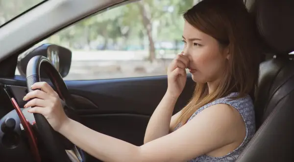Une femme pince son nez, visiblement incommodée par l'odeur de climatisation voiture.