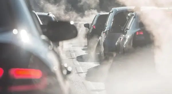 Fumée épaisse sortant de la clim de voitures dans un embouteillage. L'air est saturé de vapeur, rendant la visibilité difficile.