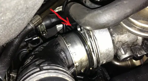 Flèche rouge pointe une durite turbo percée, suintant de l'huile dans le compartiment moteur.