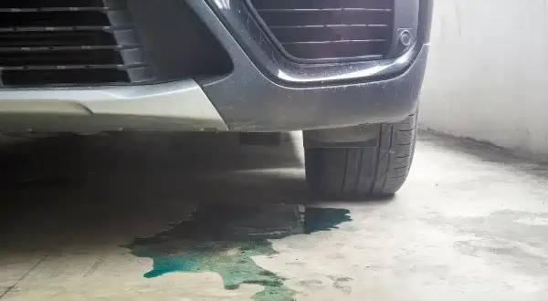 Une flaque de liquide de refroidissement couleur turquoise s'étend sous le pare-chocs d'une voiture garée.