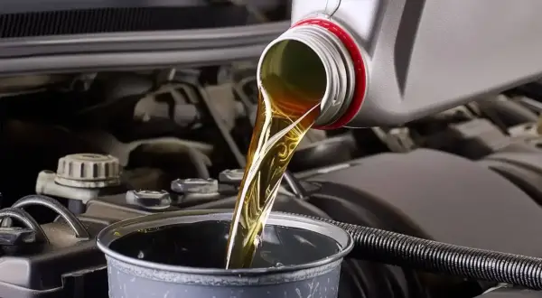 Huile moteur versée dans un entonnoir, étape clé avant la vidange par aspiration. Le moteur de la voiture est visible en arrière-plan.