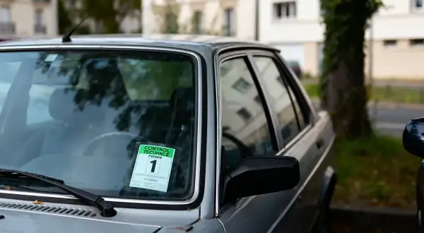 Autocollant de contrôle technique périmé 1 mois sur le pare-brise d'une voiture grise.