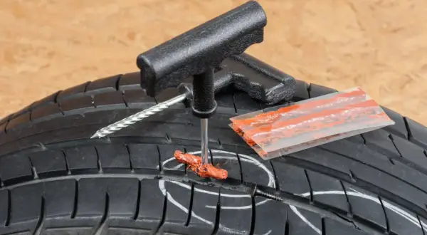 Kit de réparation pour pneu de voiture : un outil insère une mèche dans un pneu crevé, prêt à réparer.