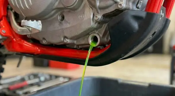 Vidange du liquide de refroidissement OAT d'une moto. Le liquide vert vif s'écoule du moteur dans un bac de récupération.