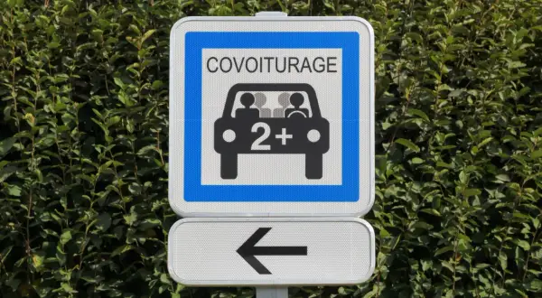 Panneau de signalisation "Covoiturage" indiquant une voie réservée aux véhicules de 2 personnes ou plus. Une flèche noire pointe vers la gauche.