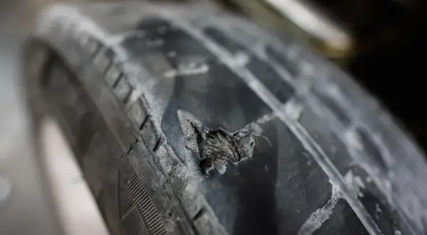 Gros plan sur une hernie sur un pneu de voiture, montrant le caoutchouc déchiré et usé. Un danger potentiel sur la route.