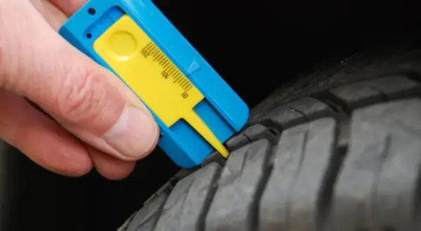 Mesure de la bande de roulement d'un pneu avec un jauge. Le résultat indique une usure trop importante, synonyme de refus contrôle technique pneu.