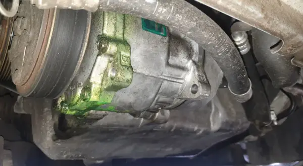Recherche fuite clim auto : le compresseur est couvert d'un liquide vert fluorescent, signe d'une fuite.