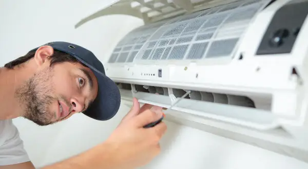 Un technicien répare une climatisation bruyante. Il utilise un tournevis pour ajuster une pièce.