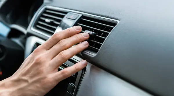 Main d'une personne ajustant la direction de l'air d'une grille de ventilation de voiture, près d'un bouton clim voiture.