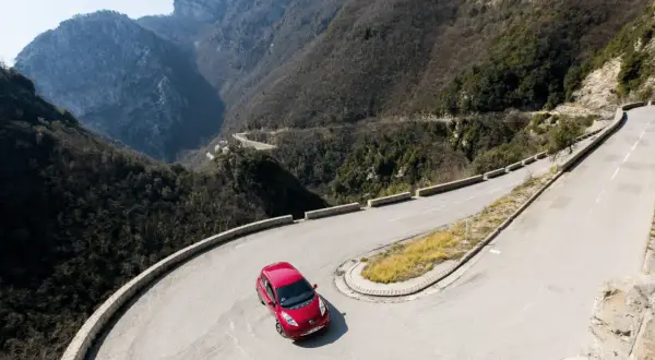Voiture rouge sur route de montagne sinueuse. Le frein moteur de la boîte automatique gère la descente.