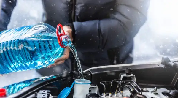 Person verse une grande bouteille de lave glace maison dans le réservoir de la voiture, sous une légère chute de neige.