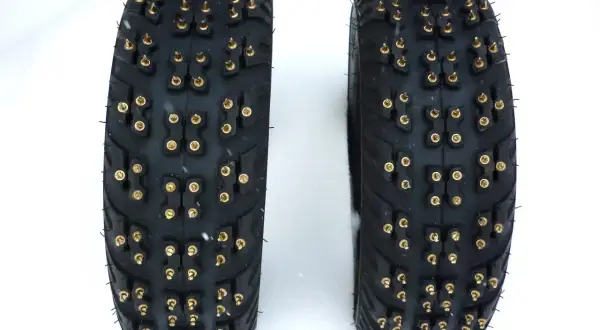 Deux pneus cloutés, prêts pour affronter les routes enneigées de France. Leurs crampons dorés promettent une adhérence maximale sur la glace.