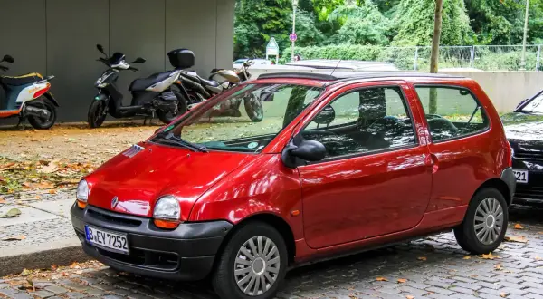Twingo 1 rouge garée sur pavés, avec des scooters et des arbres en arrière-plan. Pensez à vérifier le filtre habitacle Twingo 1 pour un air pur.
