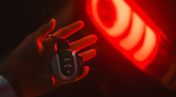 Clé de voiture Mini dans une main, éclairée par le feu arrière rouge. Une image qui évoque la recherche du prix moyen voiture occasion.