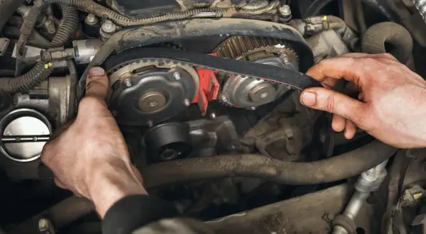 Mains d'un mécanicien ajustant la courroie de distribution essence sur un moteur de voiture.