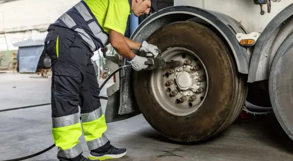 Un mécanicien en tenue de travail effectue le couple serrage roue voiture avec une clé à chocs sur un pneu de camion.