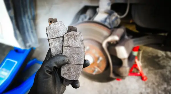 Main tenant deux plaquettes de frein usées, prêtes pour un remplacement. La graisse pour plaquette de frein est essentielle pour un bon fonctionnement.