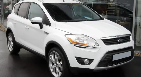 Un Ford Kuga blanc, symbole de fiabilité, garé devant un showroom.