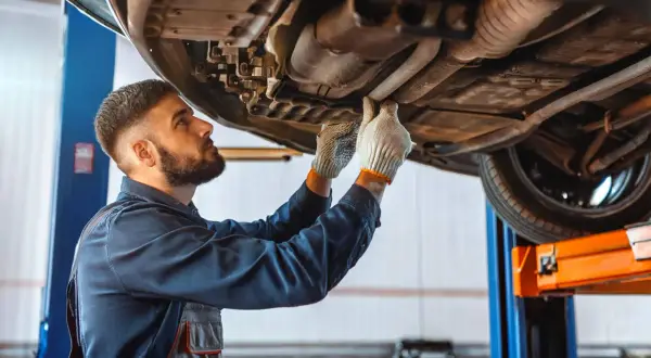 Mécanicien inspectant le dessous d'une voiture, cherchant la cause d'un embrayage bloqué en bas.