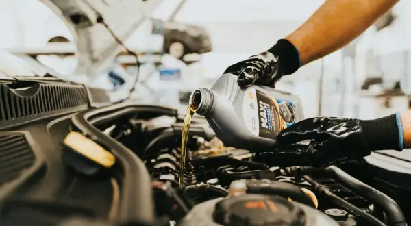 Main d'un mécanicien versant de l'huile neuve dans le moteur d'une voiture diesel. L'entretien régulier est essentiel pour la vidange de votre voiture diesel.