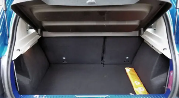Le coffre d'une Dacia Sandero, vide et propre, prêt à accueillir vos bagages. Un triangle de signalisation jaune est visible sur le côté.