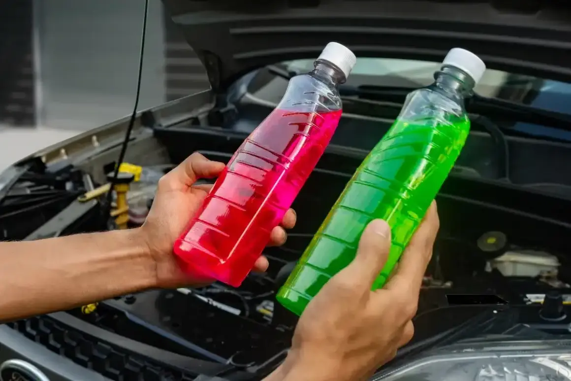 Deux bouteilles de liquide de refroidissement, une verte et une rose, sont tenues devant le moteur d'une voiture. Quel liquide de refroidissement vert pour quelle voiture ?