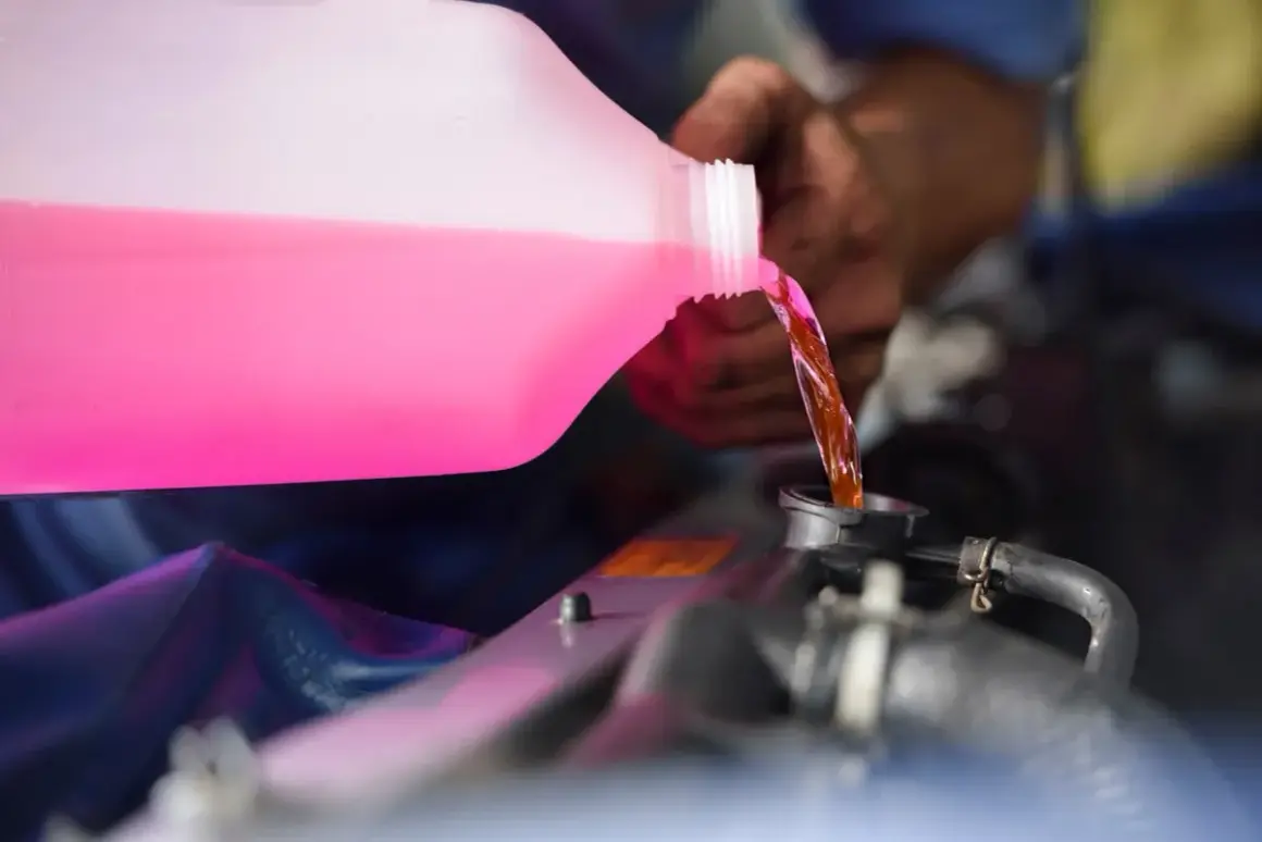 Main d'un mécanicien versant du liquide de refroidissement rose dans le radiateur d'une voiture. C'est le moment idéal pour savoir quand changer liquide de refroidissement.