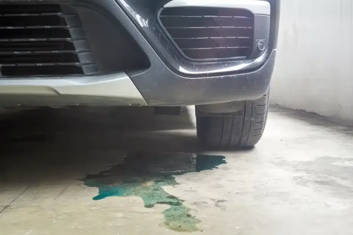 Une flaque de liquide de refroidissement couleur turquoise s'étend sous le pare-chocs d'une voiture garée.