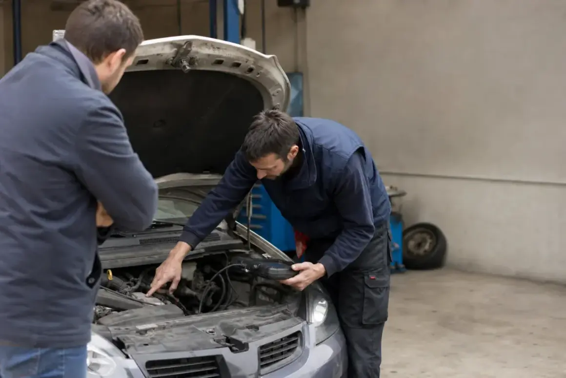 Mécanicien examinant un moteur de voiture avec un outil de diagnostic, tandis que le propriétaire écoute attentivement, espérant résoudre le bruit de ferraille quand il roule sur des bosses.