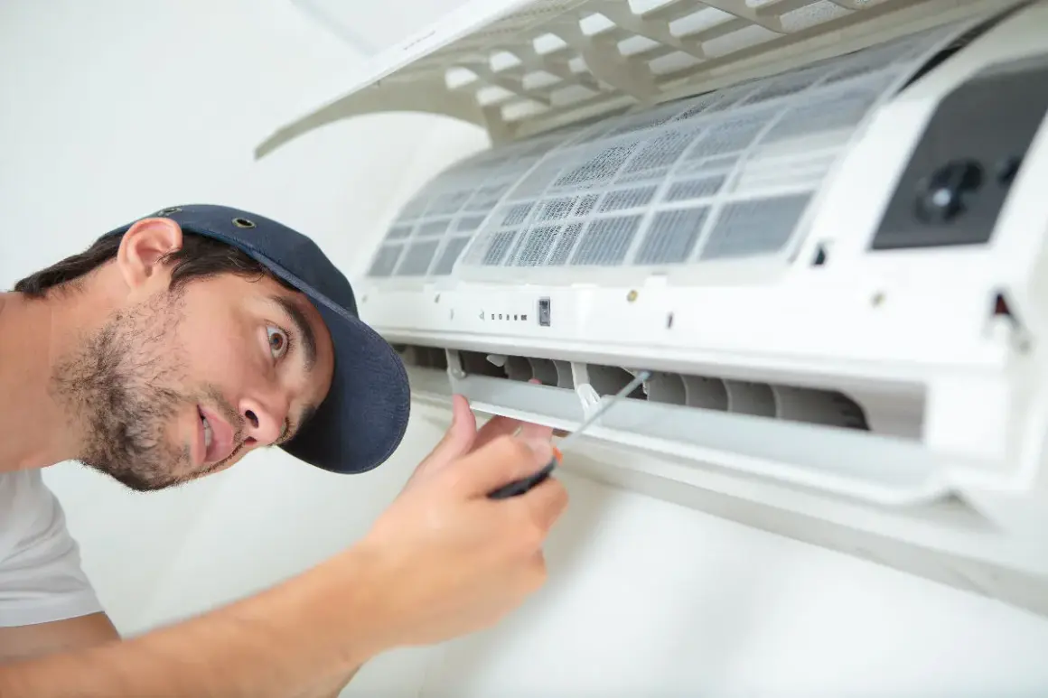 Un technicien répare une climatisation bruyante. Il utilise un tournevis pour ajuster une pièce.