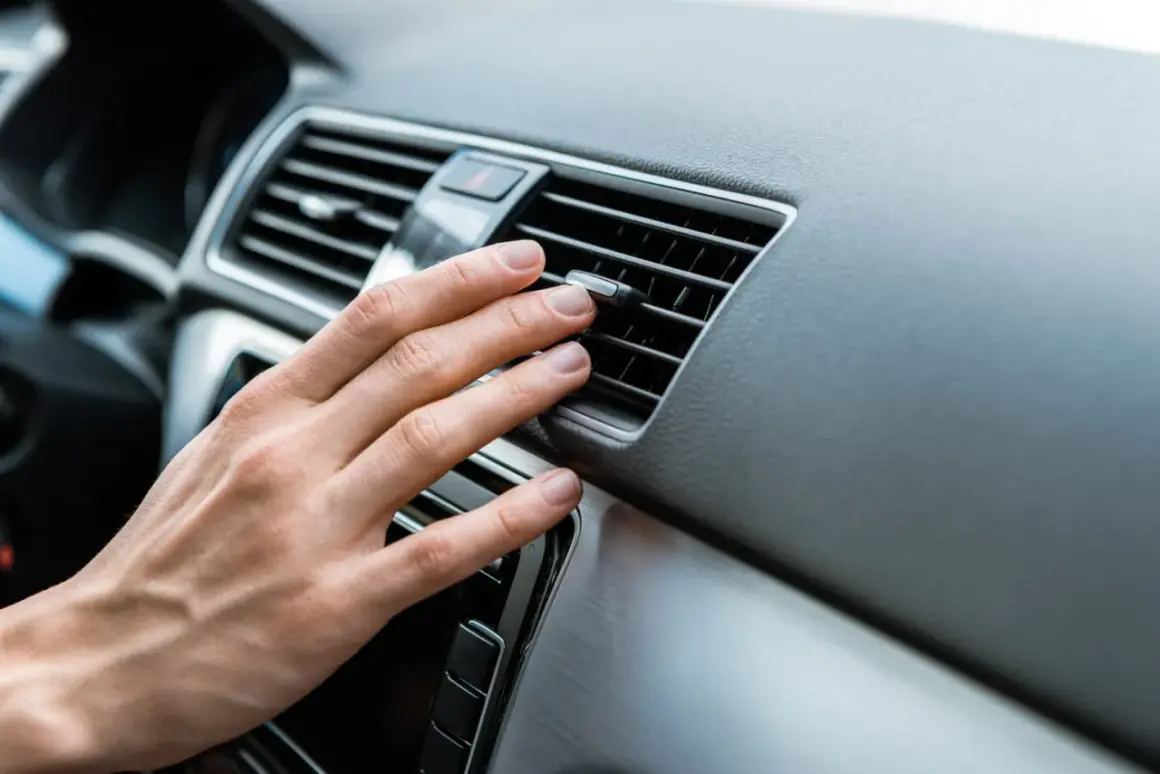 Main d'une personne ajustant la direction de l'air d'une grille de ventilation de voiture, près d'un bouton clim voiture.