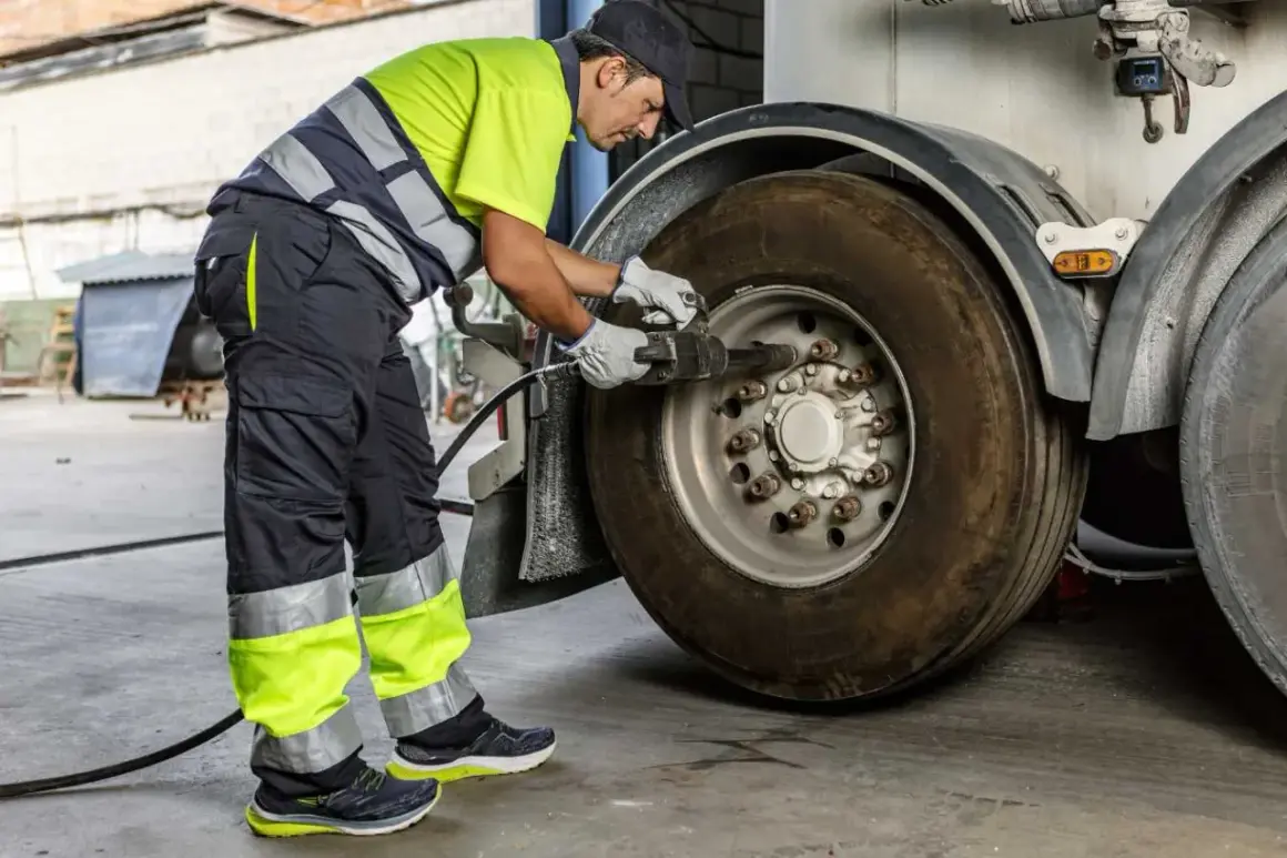 Un mécanicien en tenue de travail effectue le couple serrage roue voiture avec une clé à chocs sur un pneu de camion.