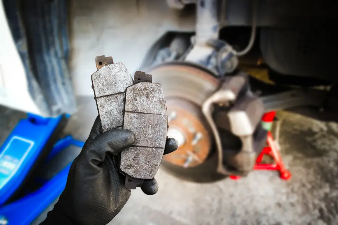Main tenant deux plaquettes de frein usées, prêtes pour un remplacement. La graisse pour plaquette de frein est essentielle pour un bon fonctionnement.