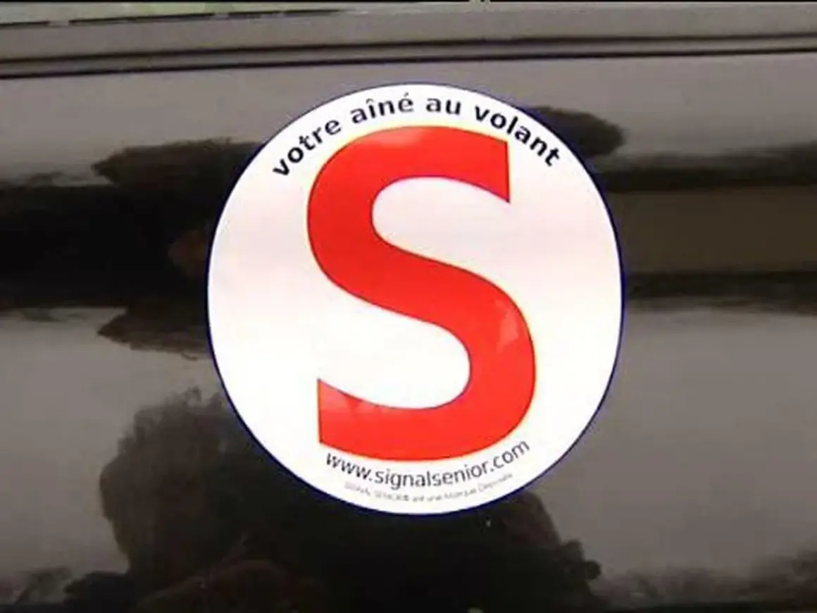 Macaron "votre aîné au volant" sur une voiture. Le S rouge est bien visible.