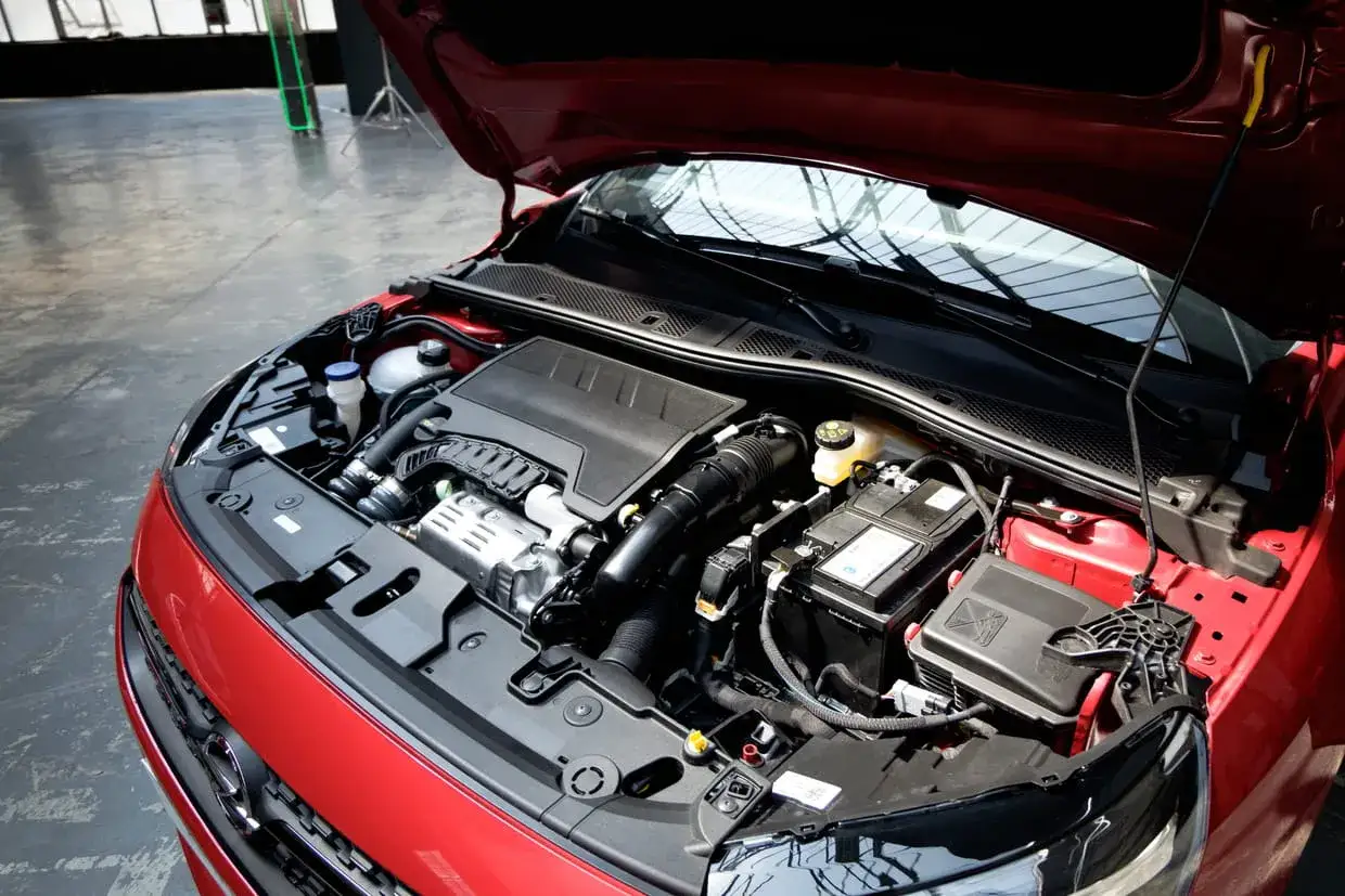 Le capot ouvert r&eacute;v&egrave;le le moteur d'une Opel Corsa rouge, avec sa batterie et ses composants bien visibles.