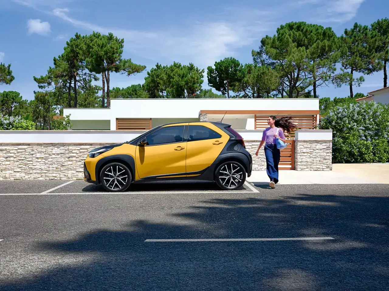Une jeune femme se dirige vers sa voiture jaune vif, une citadine automatique parfaite pour un jeune permis.