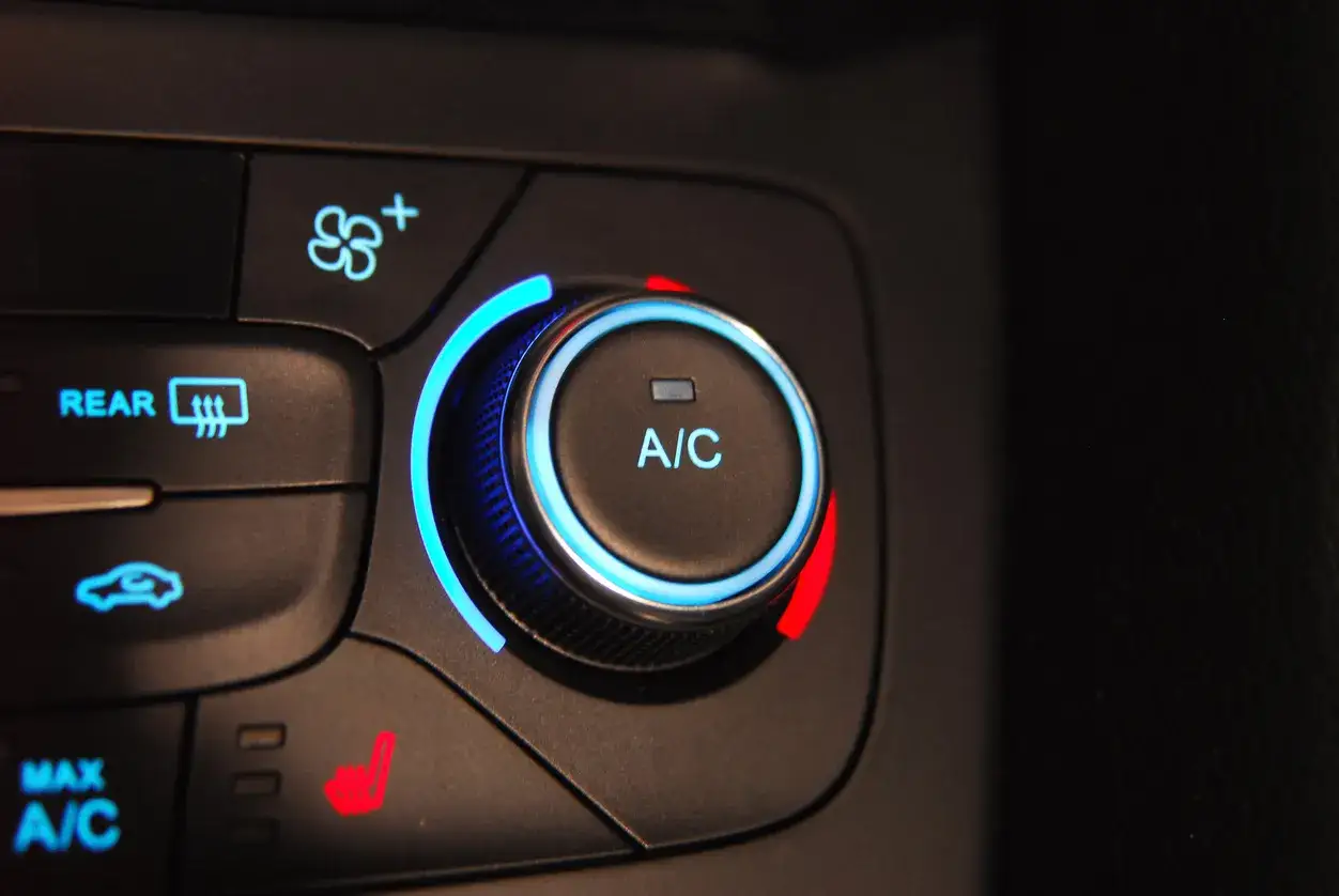 Gros plan sur le bouton clim voiture avec un anneau lumineux bleu. Icônes de désembuage arrière et de siège chauffant visibles.