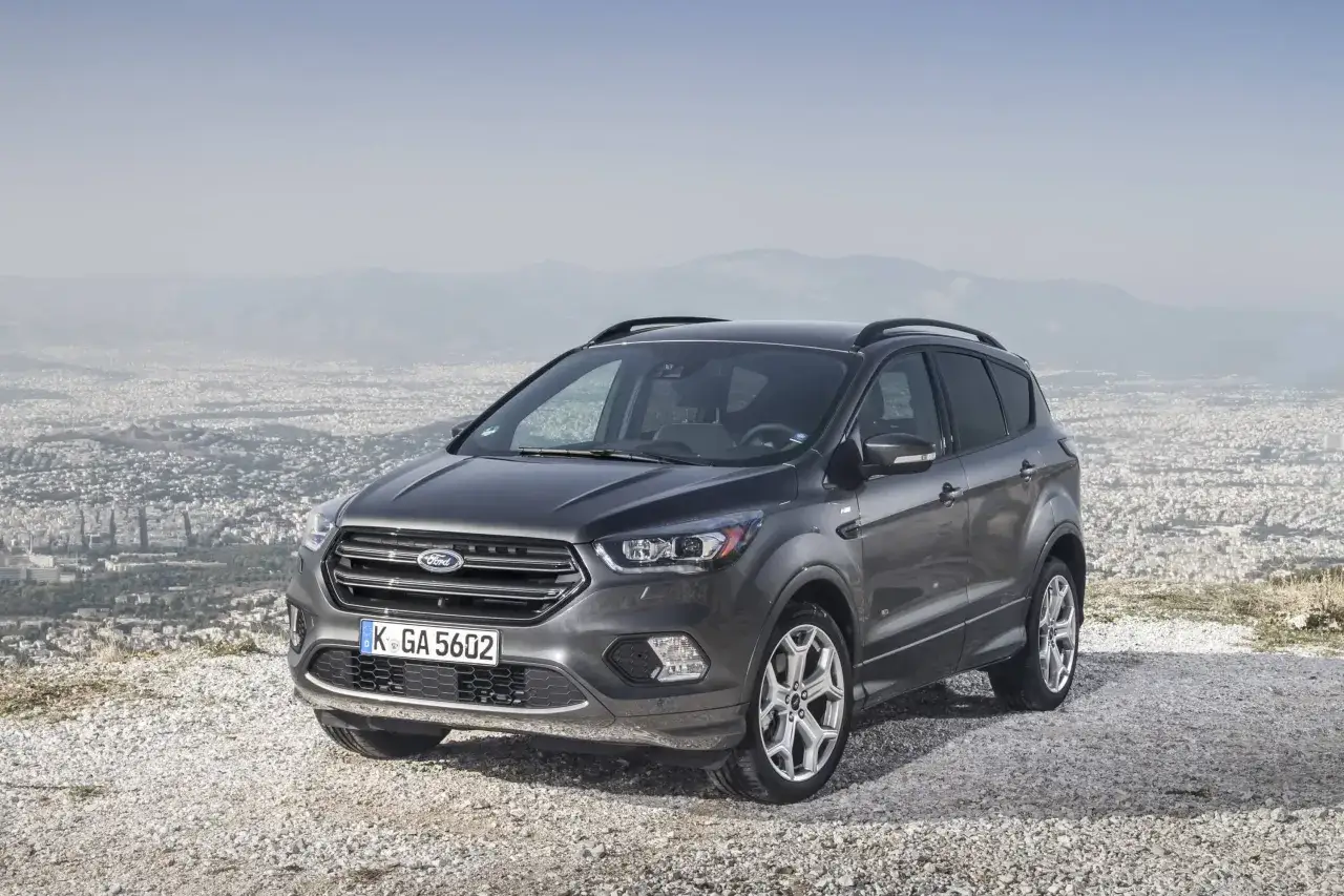 Un Ford Kuga gris, symbole de fiabilit&eacute;, stationn&eacute; sur un promontoire rocheux surplombant une ville.